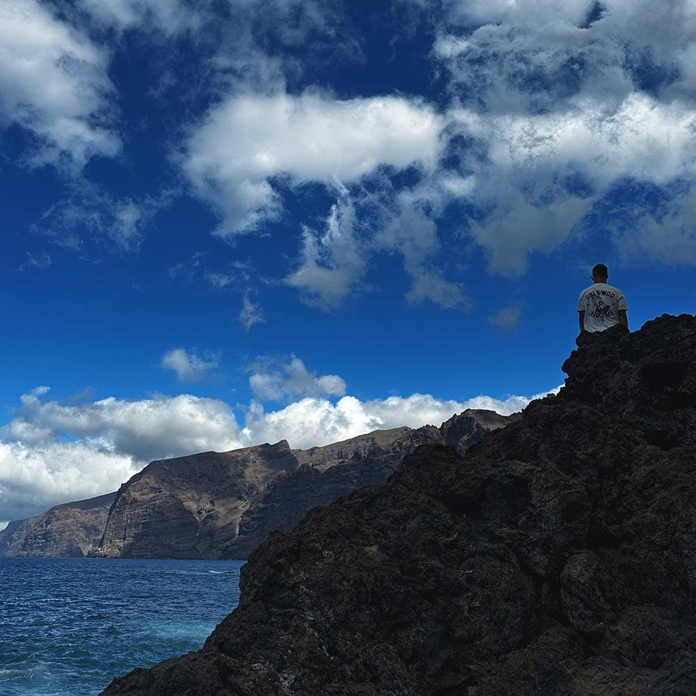 Vīrietis sēž uz akmeņiem Tenerifē ar skatu uz Los Gigantes